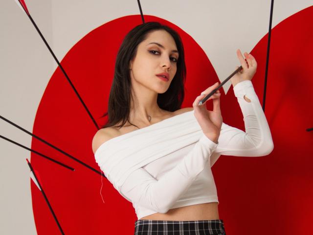 MiraPerez with dark hair, white off-shoulder top, plaid skirt, holding umbrella, red umbrella in background, looking at camera, holding umbrella handle, showing a slight smirk.