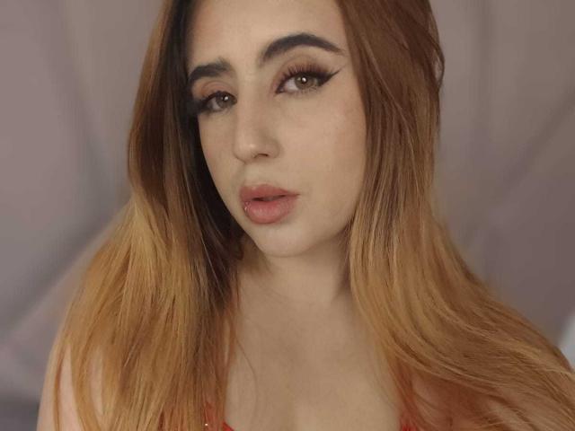 StephanieMoretti has long, ombre-colored hair, thick, dark eyebrows, and is looking at the camera with pink lips slightly parted. She's wearing a red top.