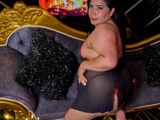 RousseBellaX in a red dress with yellow and black accents, standing in front of a large, abstract, red and black patterned design. Soft, muted colors dominate the image.