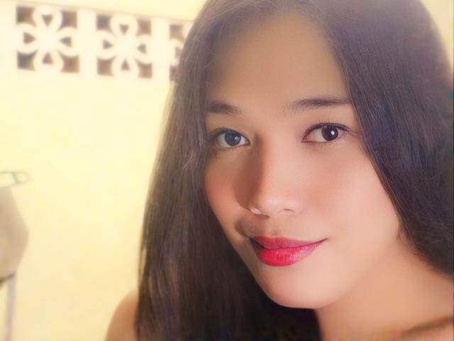 FoxyAra69 ha i capelli neri e lisci, una carnagione media e rossetto rosso. I suoi occhi sono scuri e sta sorridendo leggermente. Il seno non è visibile. Il suo viso è al centro della foto..