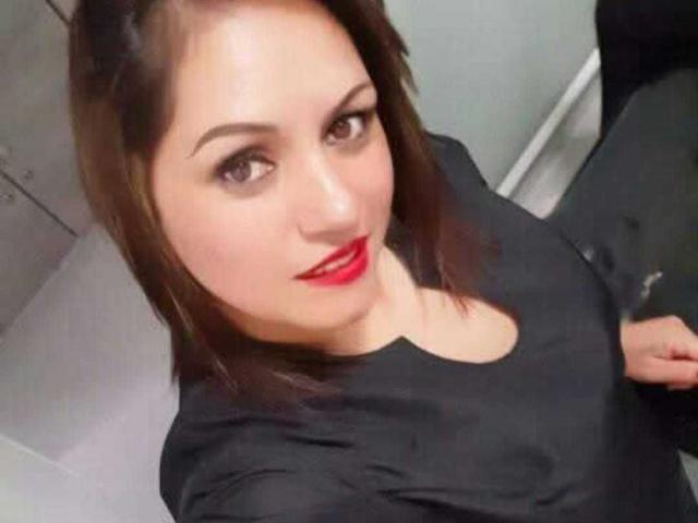 NatashaChaus has red lipstick, brown eyes, and a black shirt, with brown hair and a slight smile, showing her boobs in the selfie.