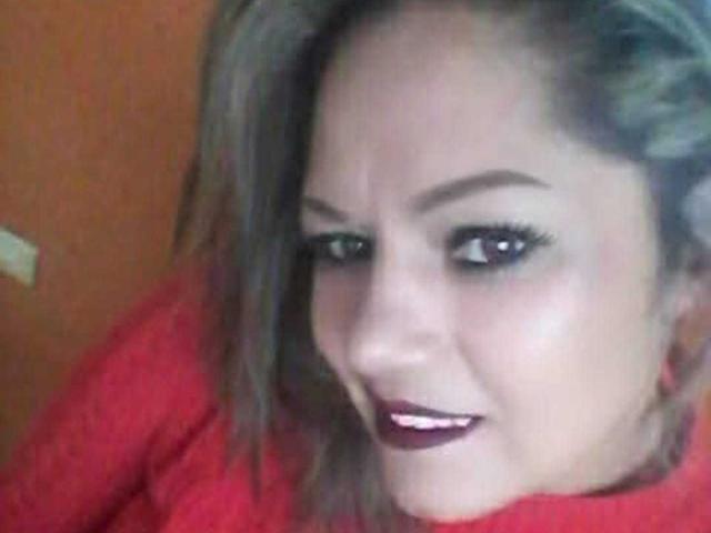 NatashaChaus with short, light brown hair, red lipstick, and black eyeliner, smiling slightly, wearing a red top, showing her teeth, and her eyes looking to the side.