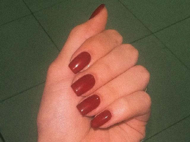 MiaHarperr's hand with shiny, red-painted nails, slightly curled fingers, and a subtle ring on the pinky. Her skin is light and smooth.