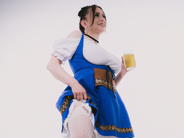 CatalinaMonyque in a blue dress with white puffy sleeves and brown belt, holding a beer mug, lifting her dress to reveal white polka-dot panties, showing her pussy.