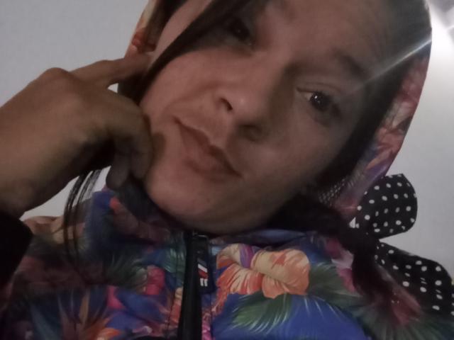 TefhaStar, con una sudadera con motivos florales, cabello castaño y una ligera sonrisa, está siendo tocada suavemente en el mentón por una mano. Su rostro está ligeramente inclinado, con una expresión relajada..