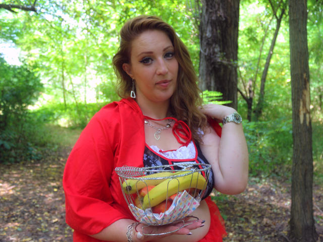 VanessaSquirtt with medium tits, red shirt, and metal basket holding bananas, standing in a forest, wearing earrings and a watch, with wavy brown hair, looking at camera.