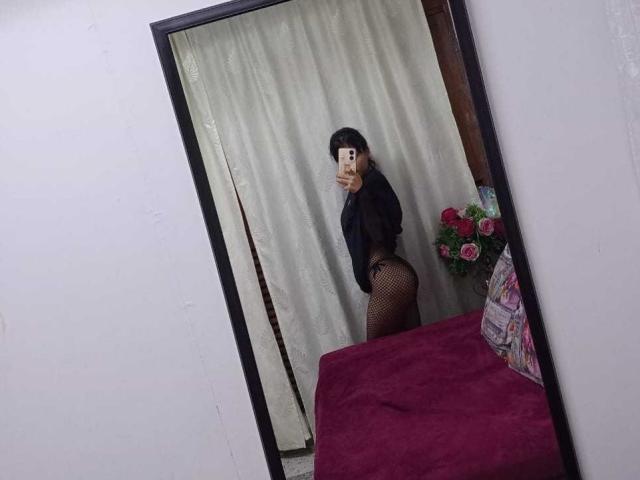 AnnieDarling's mirror selfie shows her with black fishnet pants, a black top, and her ass, holding a phone in front of white curtains. Red blanket in the foreground.