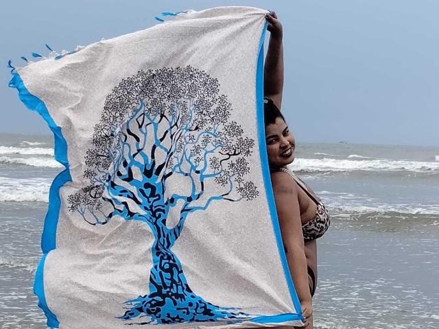 TaisaPoderosa with a blue and white flag featuring a tree design, standing in the ocean, holding the flag with one arm, wearing a leopard print bikini top.