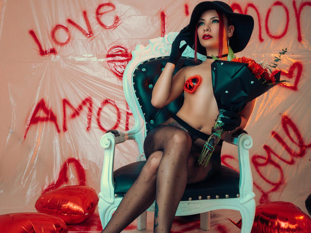 ValeryHarllow with big boobs, wearing a black hat, green jacket, heart pasties, black stockings, holding flowers, sitting on a white chair, surrounded by red balloons.