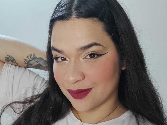AntonelaPark has dark, wavy hair, brown eyes, and bold winged eyeliner. She's wearing red lipstick, a white top, and a gold necklace, with a tattoo on her arm.