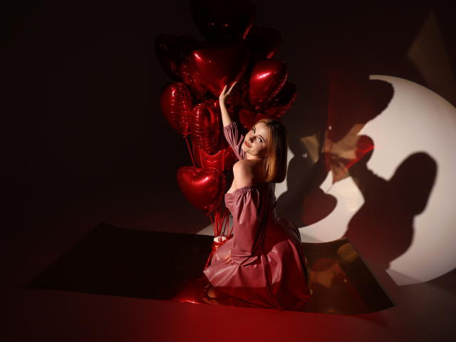 MargaritaKis with red balloons, wearing an off-shoulder pink dress, kneeling, holding heart-shaped balloons, shadow of crescent moon on wall, red light, looking back, hand on balloons.