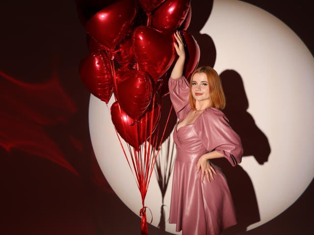 MargaritaKis met rode, hartvormige ballonnen, gekleed in een roze satijnjurk, die ze omhoog houdt, schaduw op een witte cirkel, blond haar, roze lippenstift, hand op de heup, rode touwtjes..