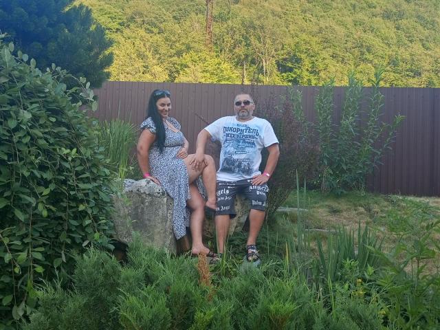 GretaTamar with big ass and small tits in a dress sits on a stone, while GretaTamar with a beer belly and small penis wears a graphic tee and shorts.