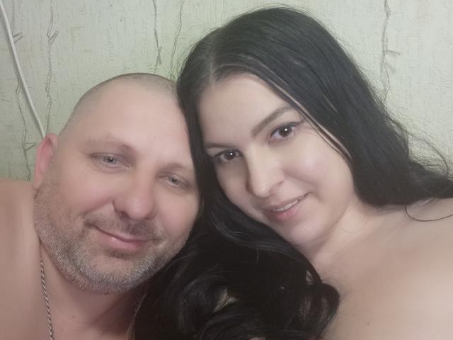GretaTamar with bald head and beard, smiling, has a chubby face and is shirtless. GretaTamar with long black hair, smiling, has a cute face and is topless.