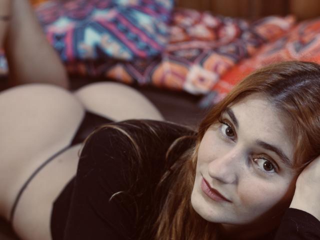 Melissadry is lying on her stomach, wearing black underwear, with her ass up and her face looking at the camera. She has long brown hair and a slight smile.