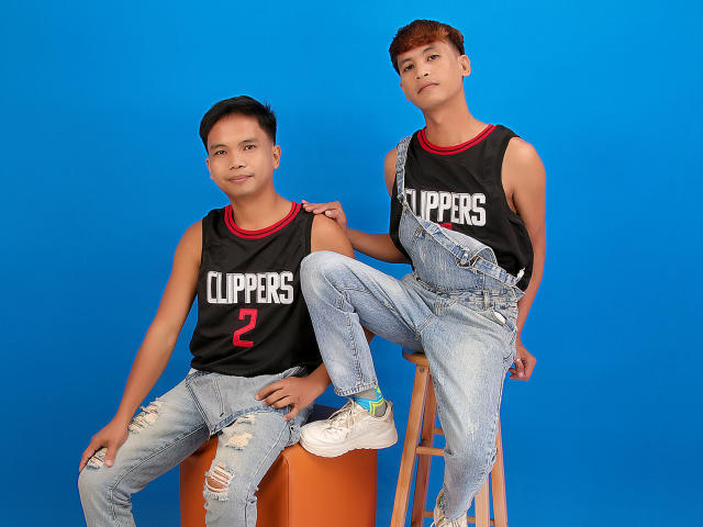 Two ExtraService69MenX, Asian, wearing black "CLIPPERS" sleeveless shirts and ripped jeans, sitting and standing with one leg on a stool, blue background. One has number "2".