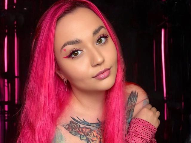 PinkHurricane-hot with bright pink hair, tattooed chest, and pink fishnet arm, brown eyes, pink lipstick, and red eyeliner, looking cute with a small red heart tattoo on her forehead.