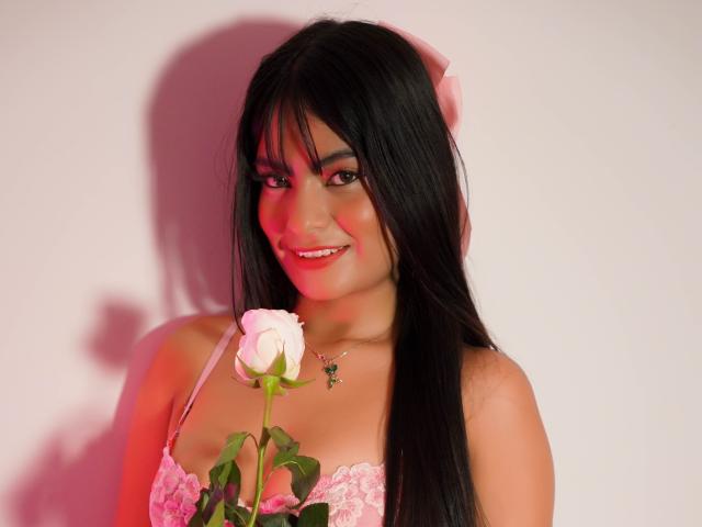 JulietaRizzo with long black hair, pink lace bra, holding a white rose, smiling, pink headband, necklace, red and pink lighting, cute, sexy, light brown skin, attractive.