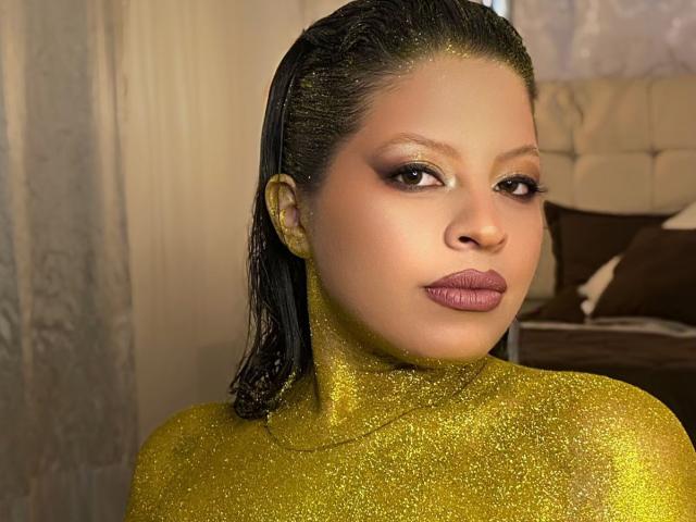 ShyVibes with shiny yellow glitter covering her neck and upper chest, black wet hair, brown eyes, and purple lipstick, looking to the side. Her ass is not visible.