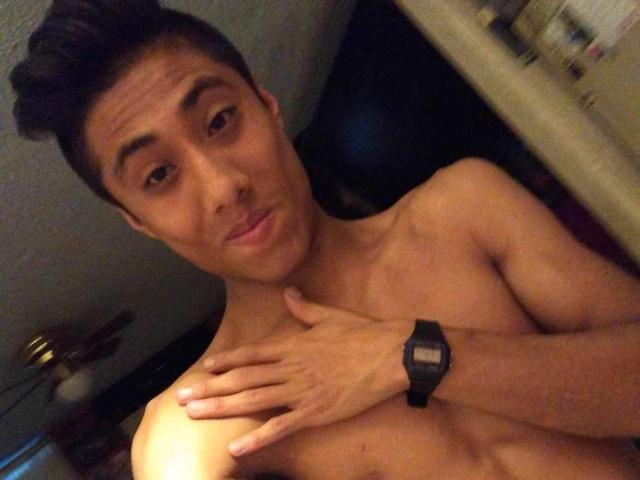 Shirtless AnthonySexyMan with short dark hair, light brown skin, and a black wristwatch, touching his collarbone with a slightly awkward, pouty expression.
