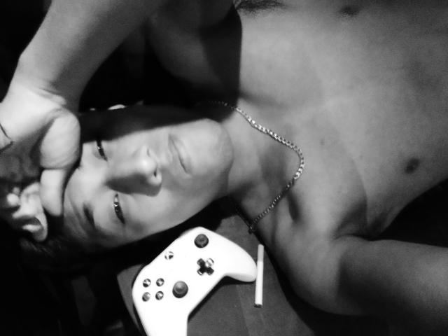 AnthonySexyMan, shirtless, lying on floor, hand on forehead, looking up, game controller on chest, necklace, grayscale, slightly blurry, medium shot, focusing on face and chest.