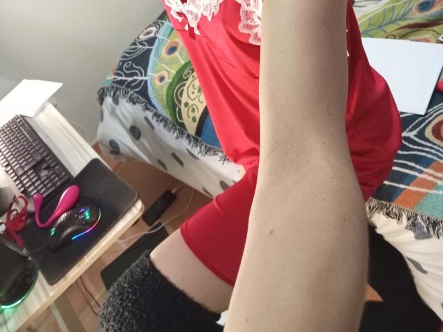 OrianaLaFrancaise's thigh and arm, wearing a red dress, black knee socks, sitting near a desk with a pink vibrator, green and blue lights, and a laptop.
