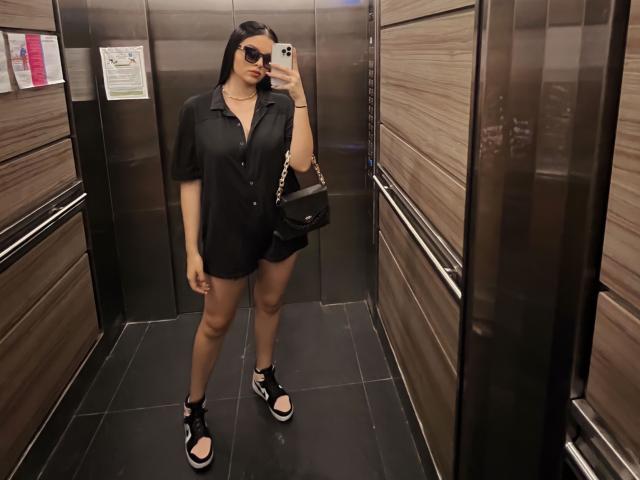 NovaDixon in a black shirt, black shorts, black shoes, holding a phone, wearing sunglasses, with a black handbag, standing in a metallic elevator. Boobs, ass, pussy not visible.