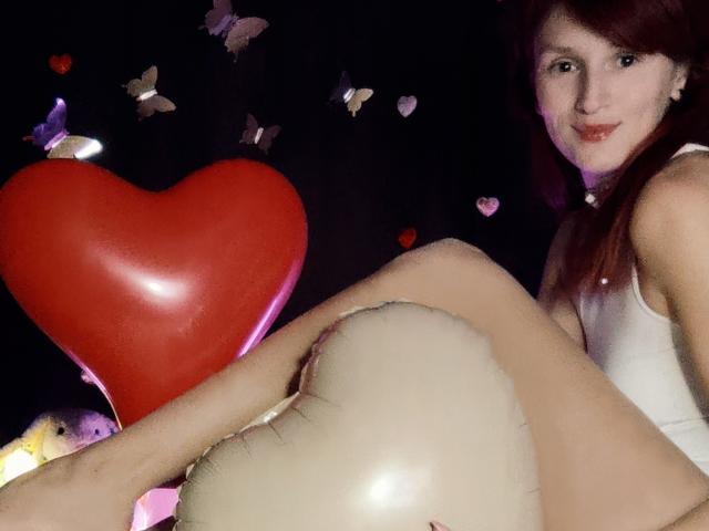 FavoriteHare com balão em formato de coração vermelho, balão branco e camiseta branca, sentada com as pernas levantadas, sorrindo para a câmera, cabelo ruivo, pele clara, fofa..