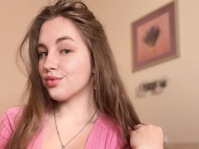 A Dooris tem cabelo castanho claro, uma camisa rosa, um sorriso discreto e está segurando o cabelo com um colar de prata. Seus seios são pequenos e ela tem um rosto bonito..