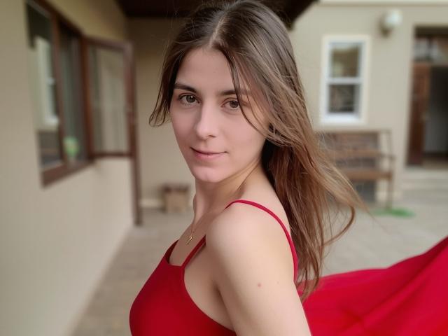 GlamMegi with long brown hair, red dress, and small tits, looking over shoulder, smiling slightly, standing on a beige balcony, light in background, soft natural light.