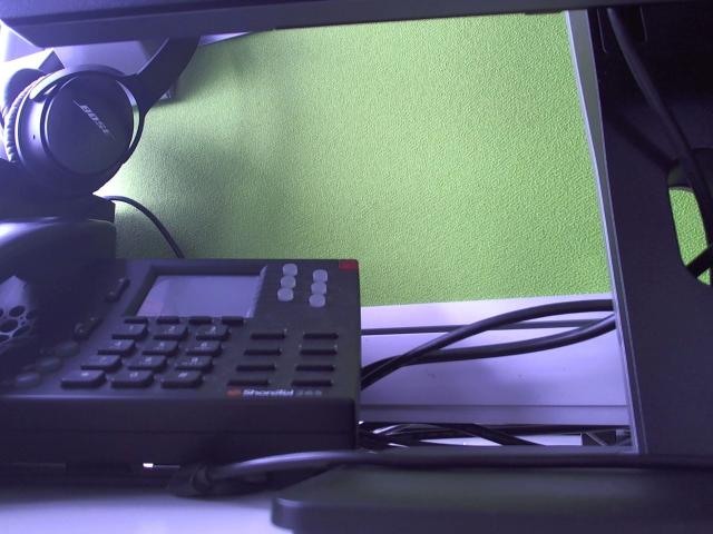 A black phone with a small screen and keypad is plugged in, next to a laptop with a green background, and black headphones are on top.