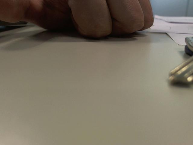 Olegator-hot's hand with a clenched fist resting on a flat, gray surface, showing knuckles and a slightly visible index finger, with a paper and pen in background.