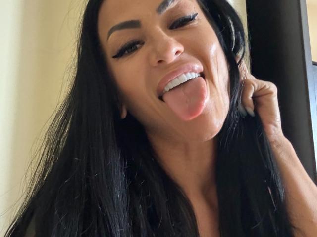 AndraD with black hair, sticking out tongue, winking, and holding hair, showing off her white teeth and subtle makeup, looking playful and sexy.