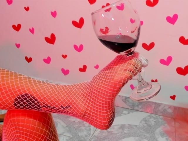 FabianaAndFabian's foot in red fishnet, holding a glass of red wine, with hearts in the background. Boobs not visible, foot and wine are the focus.