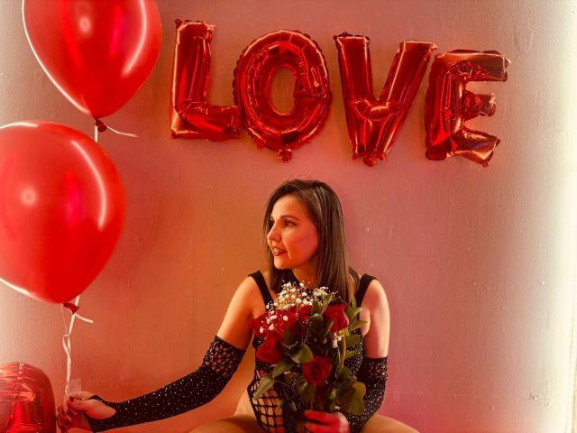 AdelaShery avec des ballons rouges, tenant des roses et un bouquet, portant des gants en filet noir, regardant sur le côté, des lettres métalliques rouges "AMOUR" en arrière-plan, lumière rose douce..