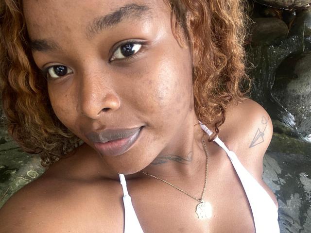MadinsonLopez has curly brown hair, dark brown eyes, and a small tattoo on her right shoulder. She's wearing a white top and a necklace with a heart-shaped pendant.