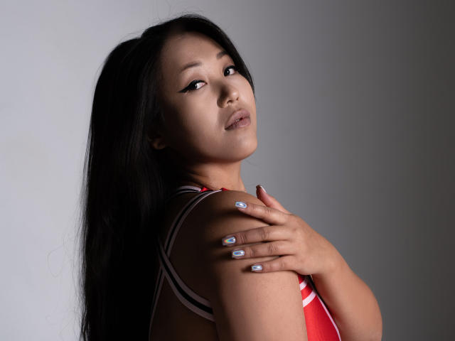 DragonDiva with long black hair, looking over shoulder, wearing a red and white striped top, hands on shoulder, blue nail polish, soft light, subtle makeup, confident expression.