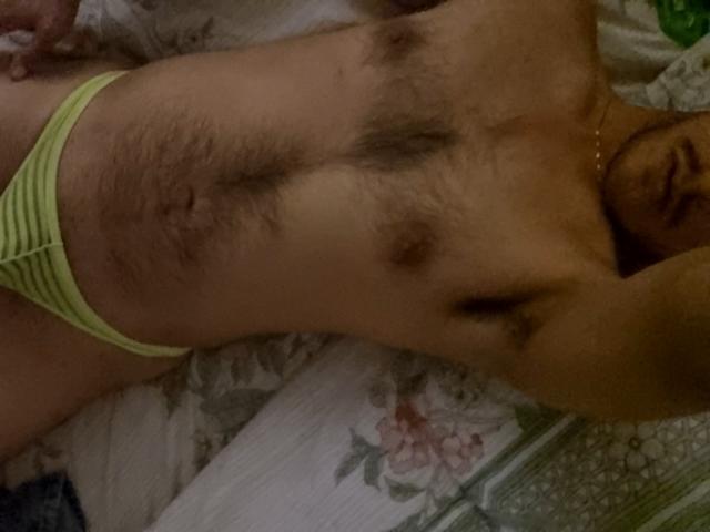 PiesoLores is lying down, wearing green striped underwear, with a hairy chest and visible armpit hair. His nipples are dark and his skin is tan.