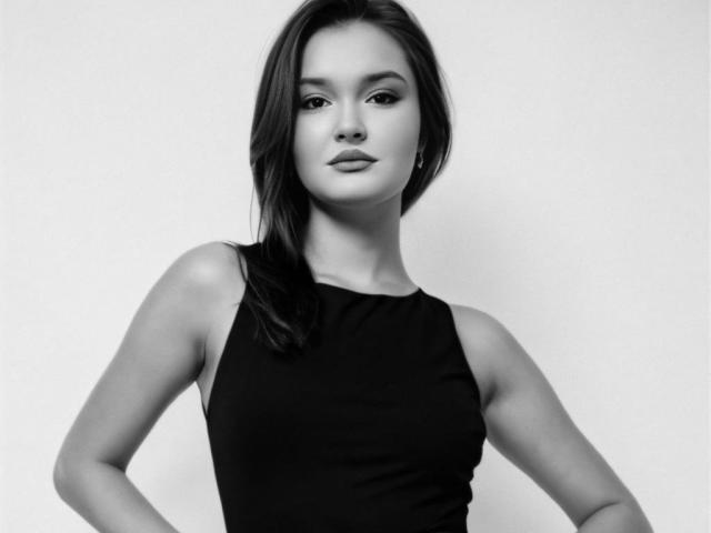 EvaLacroix with straight black hair, wearing a sleeveless black top, hands on hips, looking confident, black and white, soft light, no background. Boobs visible, face centered.