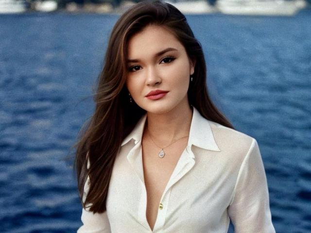 EvaLacroix with long brown hair, white button-up shirt, slight cleavage, subtle makeup, and a necklace, standing by blue water. She looks confident and attractive.