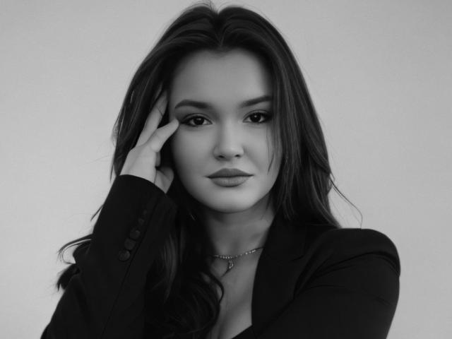 EvaLacroix with long dark hair, wearing a black blazer, touching her face, has a calm expression, grey background, and a delicate necklace. Her tits are subtle.