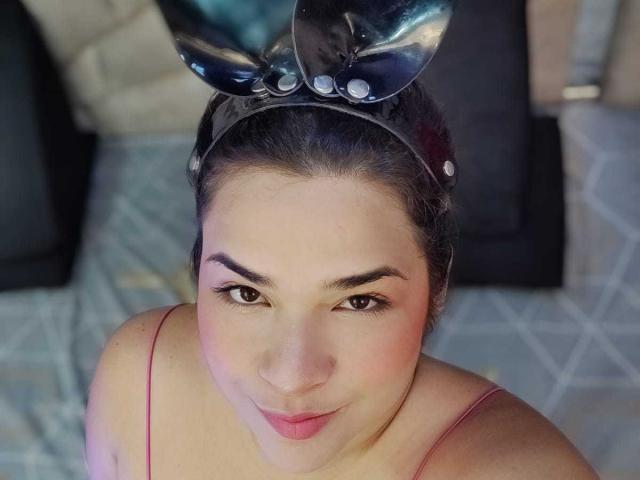 AntonelaPark with dark hair, wearing a shiny black headband with Mickey ears, pink spaghetti straps, and a cute smile, looking up with slightly flushed cheeks.