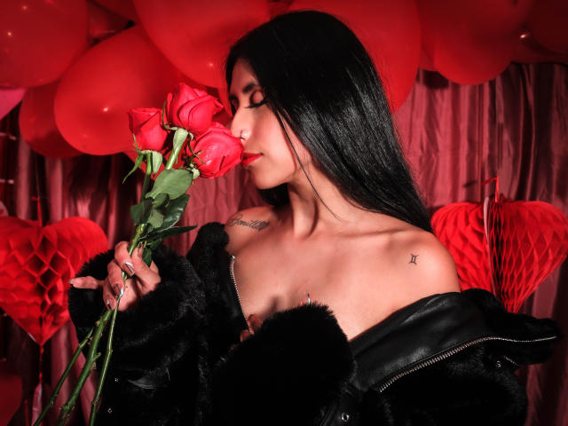 BondageGirlKs with long black hair, black fur jacket, and red roses, kissing a rose, tattoo on right shoulder, star tattoo on left shoulder, and a nipple piercing.