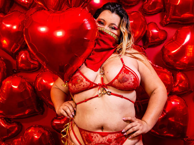 SalmaAzaman in red lingerie, sheer bra with red stains, red heart-shaped balloon in front, red face mask with gold trim, blonde hair, hands on hips, red balloons everywhere.