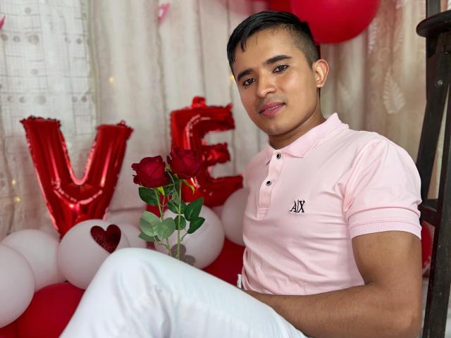 DayanWilly mit kurzen, schwarzen Haaren, heller Haut und einem süßen Lächeln, trägt ein pinkes Polohemd und weiße Hosen und sitzt mit einer roten Rose und roten Luftballons..
