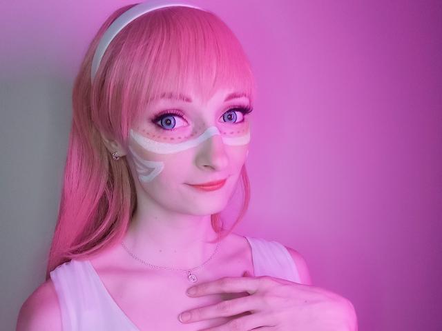 AmazingBlair with pink hair, white mask, blue eyes, and white dress, touching chest, pink and purple lighting, smiling. Boobs not visible, focus on face and upper body.