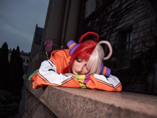 AmazingBlair with red and white hair, eyes closed, resting head on orange and white jacket, arms folded, on a stone ledge, looking tired.