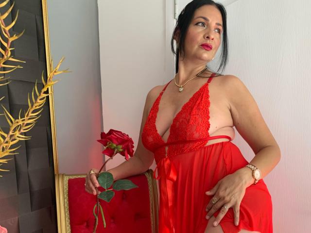 AlizonMoreti with dark hair, red lace lingerie, and a red rose, standing, looking up, holding rose, wearing gold necklace and watch, sexy, curvy, medium tits, red dress.