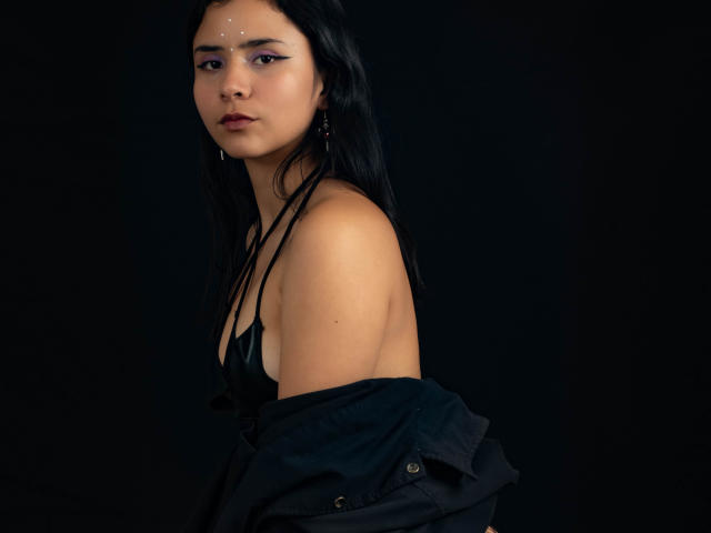 YanNyan a les cheveux noirs, un visage sérieux, une peau claire, et porte un haut noir avec une veste que porte sur ses épaules, laissant apparaître ses épaules nues et une discrète marque sur son visage..