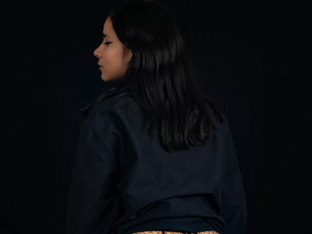 YanNyan met donker zwart haar, gekleed in een marineblauwe blouse, profiel naar links gericht, donkere achtergrond, subtiel licht op het gezicht, zachte en kalme uitdrukking..